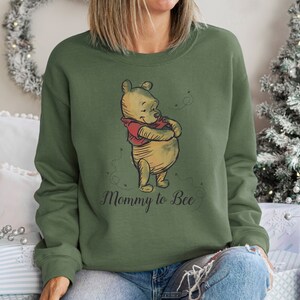 May include: A green sweatshirt with a Winnie the Pooh illustration and the text "Mommy to Bee".