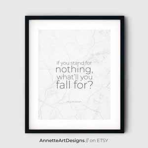 May include: A white marble background with a black framed print featuring a quote from the musical Hamilton: "If you stand for nothing, what'll you fall for?"