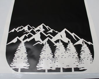May include: A black and white vinyl decal featuring a mountain range and evergreen trees. The design is a silhouette of the natural landscape, with the trees in the foreground and the mountains in the background. The decal is likely for a car or wall.