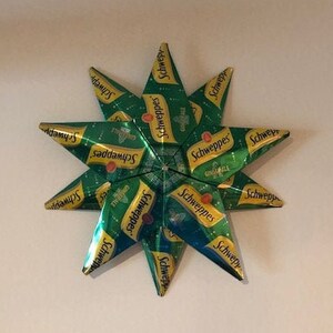May include: A green and gold star-shaped ornament made from recycled Schweppes soda cans.