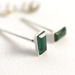May include: A pair of silver stud earrings with emerald green rectangular gemstones.