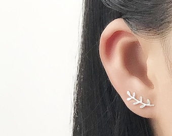 May include: Silver leaf earrings with a delicate branch design. The earrings are shown on a model's ear.