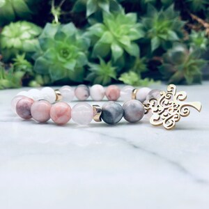May include: A bracelet made with pink, white and grey beads with a gold tree charm.