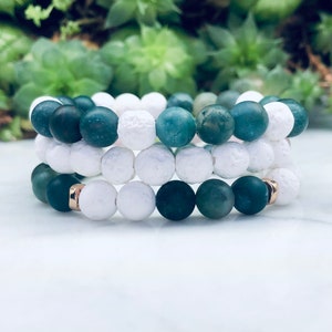 May include: Three stacked bracelets featuring white lava rock beads and green agate beads. The bracelets are displayed on a white surface.