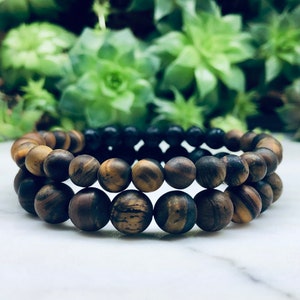 May include: Two beaded bracelets, one with brown and gold tiger's eye beads and the other with black beads.