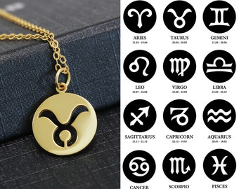 May include: Gold necklace with a pendant featuring a cutout of the Taurus zodiac sign. The pendant is round and has a smooth, polished finish. The necklace is on a black background with a chart of the zodiac signs and their dates.