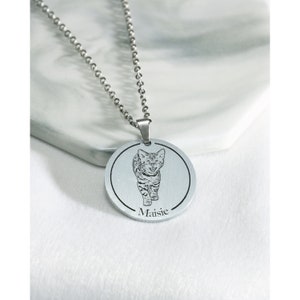 Pu&ograve; includere: Collana d'argento con un ciondolo rotondo che presenta un'immagine incisa in bianco e nero di un gatto. Il ciondolo ha il nome "Maisie" inciso sotto l'immagine.