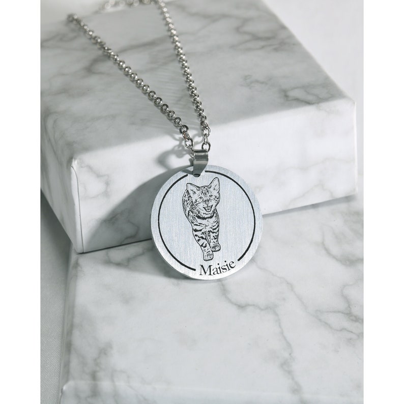 Pu&ograve; includere: Una collana d'argento con un ciondolo rotondo che presenta una foto in bianco e nero di un gatto. Il ciondolo &egrave; inciso con il nome "Maisie".