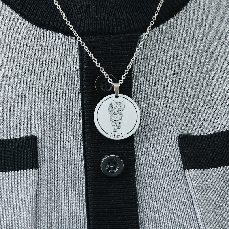 Pu&ograve; includere: Una collana d'argento con un ciondolo rotondo che presenta una foto in bianco e nero di un gatto. Il ciondolo &egrave; inciso con il nome "Maisie".