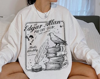 May include: White sweatshirt with a black and white graphic print of a raven, books, and a quill. The text on the graphic reads "The Edgar Allan Poe-Try Club" and "still I read on".