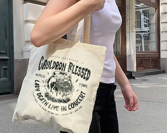 May include: A white tote bag with a black graphic design featuring a cauldron, flames, and the text "Gesta Balchora is Cauldron Blessed World Tour Lady Death Live in Concert".