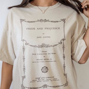 May include: A beige t-shirt featuring a black graphic print of the book cover for "Pride and Prejudice" by Jane Austen. The book cover has a decorative border with floral accents and the text "Edited with Introduction and Notes by Frank Sich, Jr."