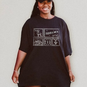 May include: A black oversized t-shirt with a graphic print of four postage stamps featuring a deer, a castle, a gate, and a unicorn. The text "TERRASEN" is printed on one of the stamps.