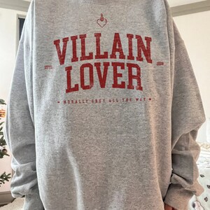 May include: Grey sweatshirt with a red graphic print that says "VILLAIN LOVER" with the text "ESTD 2008" and "MORALLY GREY ALL THE WAY" underneath.
