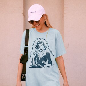 May include: A light blue t-shirt with a vintage illustration of a woman reading a book. The text on the shirt reads "I can't I have a date with my book boyfriend tonight."