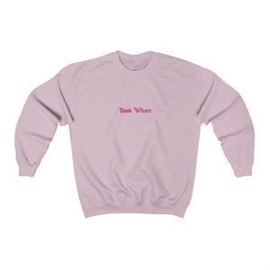 Puede incluir: Una sudadera de color rosa claro con el texto "Book Whore" en rosa.