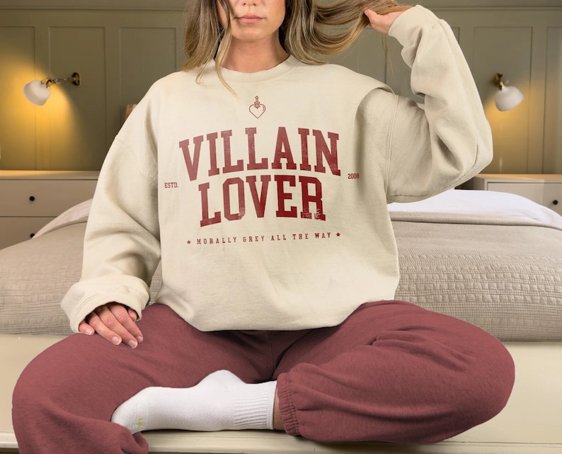 May include: A cream-coloured sweatshirt with a red graphic that says "VILLAIN LOVER" with the text "ESTD. 2008" and "MORALLY GREY ALL THE WAY" in smaller font.