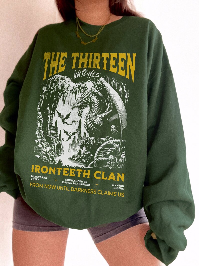 Pu&ograve; includere: Felpa verde con una stampa grafica di un drago in una grotta. Il testo "The Thirteen Witches Ironteeth Clan" &egrave; stampato sulla parte anteriore della felpa. Il testo "Commanded by Manon Blackbeak" e "From now until darkness claims us" &egrave; anche stampato sulla felpa.