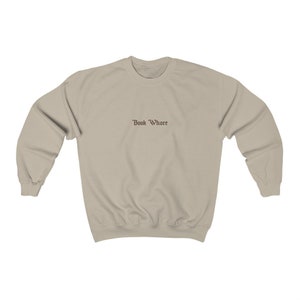 Puede incluir: Una sudadera de color beige claro con el texto "Book Whore" impreso en marr&oacute;n en la parte delantera.