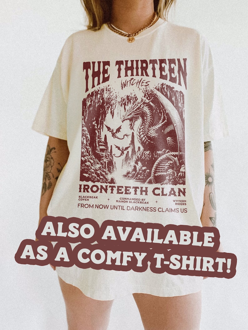 Pu&ograve; includere: Una t-shirt bianca con una stampa grafica bordeaux di un drago e il testo "The Thirteen Witches Ironteeth Clan From Now Until Darkness Claims Us" sul davanti. Il testo "Also Available As A Comfy T-Shirt!" &egrave; stampato in un grande font sotto la grafica.