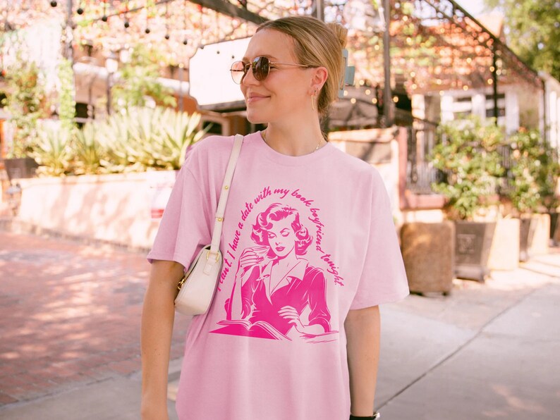 May include: Pink t-shirt with a graphic of a woman reading a book and the text "Can't I have a date with my book boyfriend tonight?"
