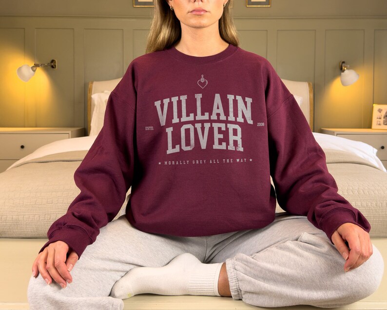 May include: A maroon sweatshirt with the text "Villain Lover" in white, with a small heart and dagger graphic above the text. The text "Morally Grey All The Way" is printed below the main text.