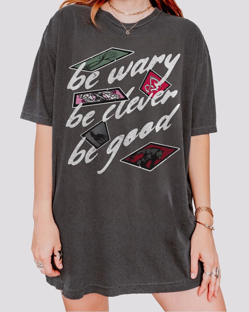 Puede incluir: Una camiseta gris oscuro con un estampado gr&aacute;fico de estilo vintage que dice "be wary be clever be good". El gr&aacute;fico presenta una serie de im&aacute;genes en forma de diamante con varias ilustraciones.