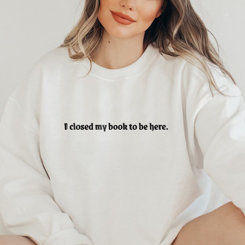 Peut inclure: Sweat-shirt blanc avec le texte "J'ai ferm&eacute; mon livre pour &ecirc;tre ici."
