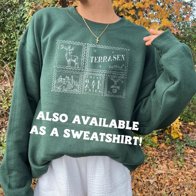 May include: A dark green sweatshirt with a white graphic print of four postage stamps. The stamps feature a deer, a castle, a text design, and a design with the words "To Wherever You Go". The text "Terrasen" is printed on the sweatshirt. The text "ALSO AVAILABLE AS A SWEATSHIRT!" is printed below the graphic.