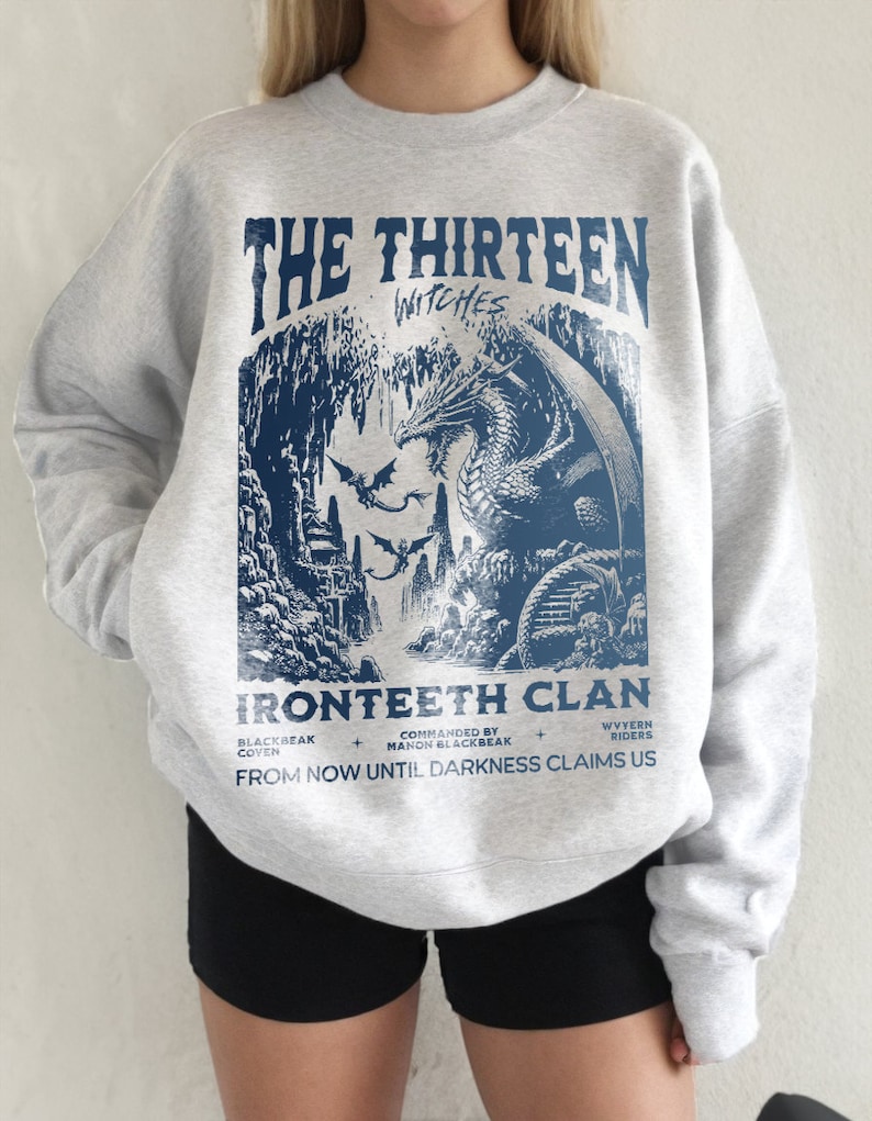 Pu&ograve; includere: Felpa grigia con una stampa grafica di un drago in una grotta. Il testo sulla felpa recita "The Thirteen Witches Ironteeth Clan Blackbeak Coven Commanded by Manon Blackbeak Wyvern Riders From Now Until Darkness Claims Us."