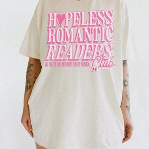 May include: A white t-shirt with a pink graphic that says "Hopeless Romantic Readers Club" with a pink heart and a pink bow. The text says "We prefer our men written by women."