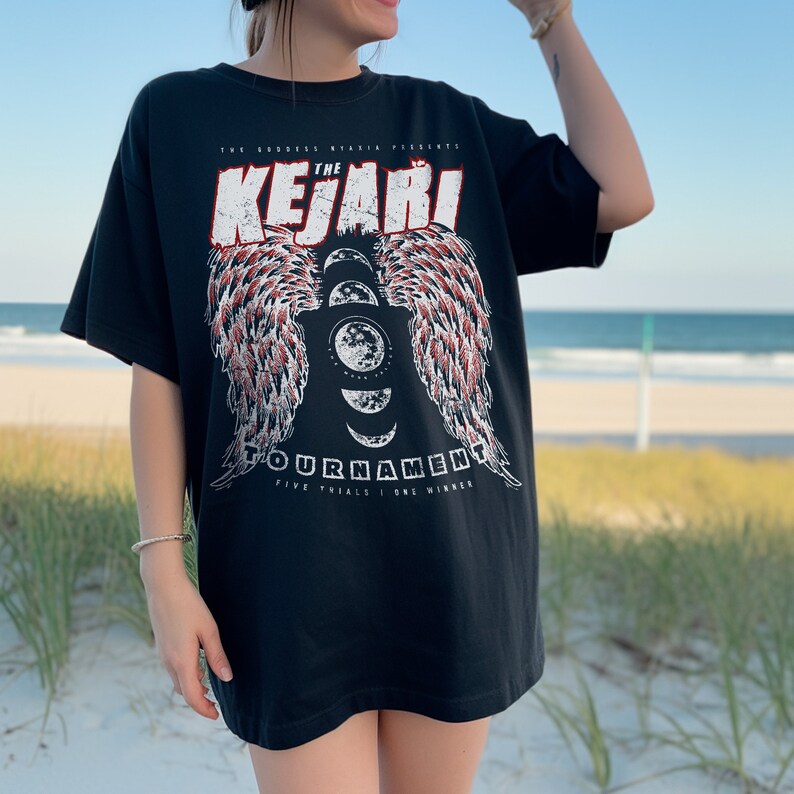 May include: Black t-shirt with a graphic print of a winged moon with the text "The Goddess Ryankia Presents The Kejari Tournament Five Trials | One Winner"