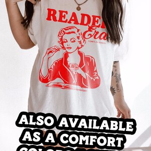 May include: White t-shirt with a red graphic of a woman reading a book and the text "Reader Era I Can't, I'm Booked". The text "ALSO AVAILABLE AS A COMFORT COLORS T-SHIRT!" is at the bottom of the image.