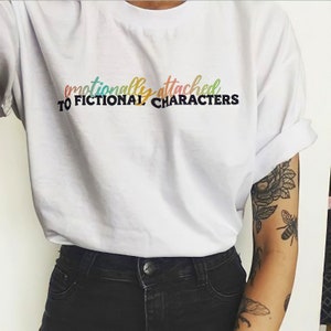 May include: White t-shirt with the text "emotionally attached to fictional characters" in rainbow colors.