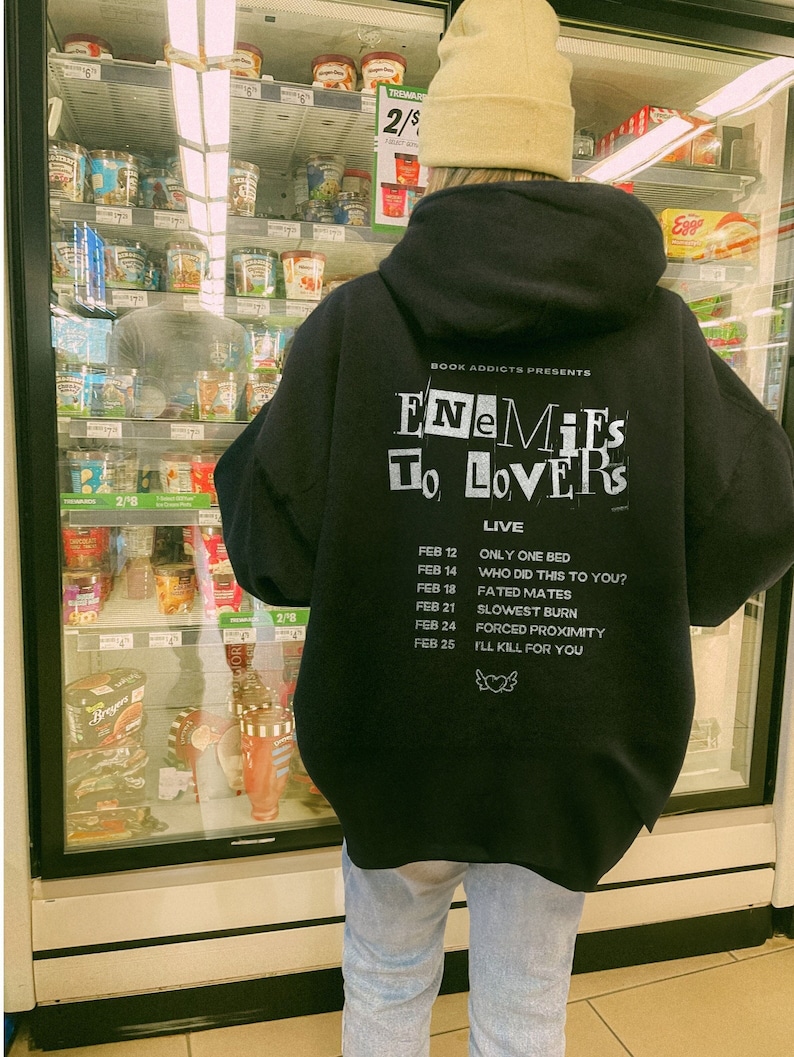 Peut inclure: Un sweat &agrave; capuche noir avec du texte blanc qui dit "Enemies to Lovers Live". Le sweat &agrave; capuche liste &eacute;galement plusieurs dates et titres de chansons. La personne porte un bonnet beige et un jean bleu clair.