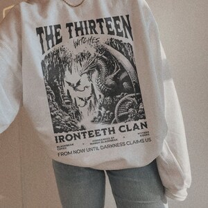 Pu&ograve; includere: Felpa bianca con una stampa grafica in bianco e nero di un drago e un testo che recita "The Thirteen Witches Ironteeth Clan Blackbeak Coven Commanded by Manon Blackbeak Wyvern Riders From Now Until Darkness Claims Us"