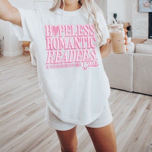 May include: White t-shirt with pink text that reads "Hopeless Romantic Readers Club" and "We prefer our men written by women".
