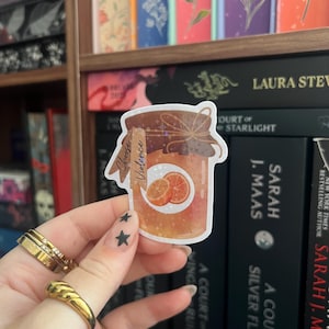 Op de afbeelding: Een sticker met een pot sinaasappelmarmelade met de tekst "Choose Violence". De pot is bruin met een etiket en een strik. De achtergrond toont een boekenplank met boeken.