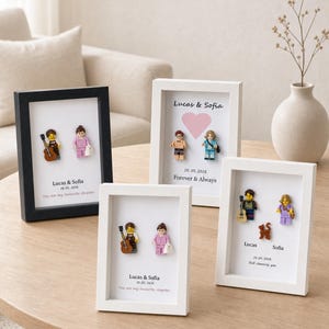 Könnte beinhalten: Vier rechteckige Schattenfugenrahmen mit individuellen Kunststoff-Minifiguren. Jeder Rahmen enthält gedruckten Text, darunter Namen wie Lucas & Sofia, Daten und Phrasen wie You are my favourite chapter, Forever & Always und Still choosing you.