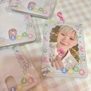 May include: Clear plastic photo card holder with a photo of a person holding a pink flower. The holder has a decorative border with the word "love" in colorful letters. A pink beaded keychain is attached.