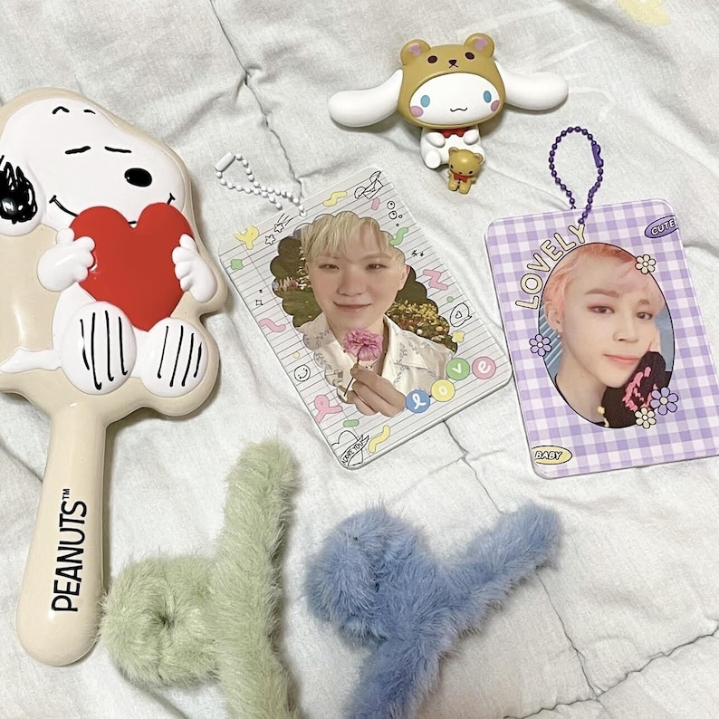 May include: An assortment of items including a Snoopy brush holding a red heart, two photo cards with images of people, a brown bear figurine, a white and brown cartoon character, and two fluffy hair clips in green and blue.