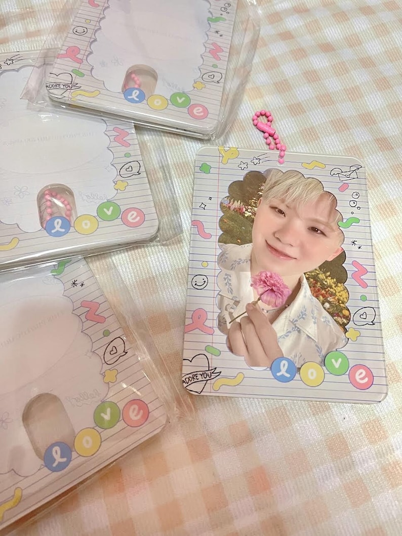 May include: Clear plastic photo card holder with a photo of a person holding a pink flower. The holder has a decorative border with the word "love" in colorful letters. A pink beaded keychain is attached.