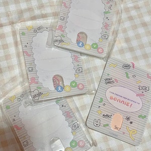 May include: Four clear plastic photocard holders with a white and pastel design. Each holder has a scalloped edge and a slot for a photocard. One holder reads "THIS PHOTOCARD BELONGS TO BONNIE!" with the word "BONNIE!" in pink.