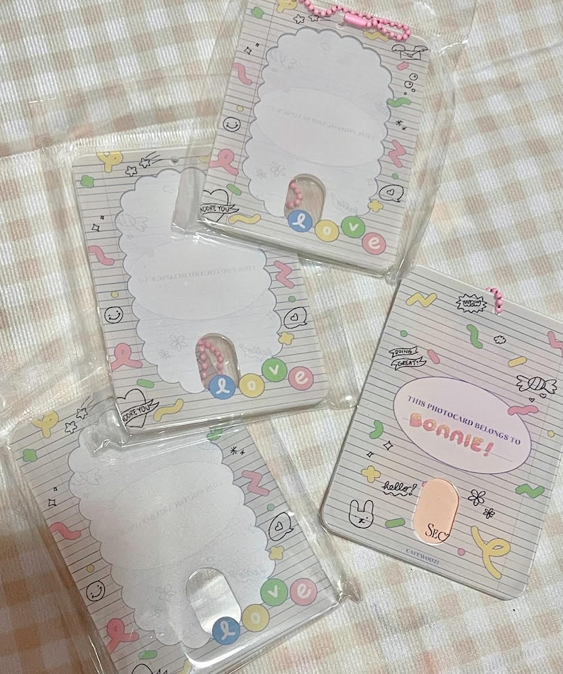 May include: Four clear plastic photocard holders with a white and pastel design. Each holder has a scalloped edge and a slot for a photocard. One holder reads "THIS PHOTOCARD BELONGS TO BONNIE!" with the word "BONNIE!" in pink.