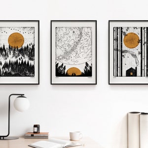 Puede incluir: Tres impresiones enmarcadas en negro con fondos blancos e ilustraciones en blanco y negro. Las impresiones presentan una escena de bosque con un sol dorado, un mapa de constelaciones con un sol dorado y una escena de bosque con un sol dorado y una peque&ntilde;a casa.