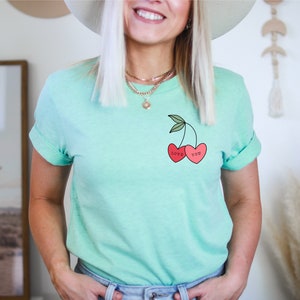 Pode incluir: Uma camiseta verde claro com um gráfico de duas cerezas vermelhas. As cerejas têm as palavras "Love" e "You" escritas nelas.