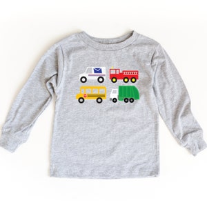 May include: A gray long-sleeved t-shirt with a graphic of four different vehicles: a mail truck, a fire truck, a school bus, and a garbage truck.