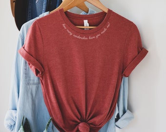 Könnte beinhalten: Ein rotes T-Shirt mit dem Text "Wie viele Sandwiches hast du mir gemacht?" auf der Vorderseite gestickt.