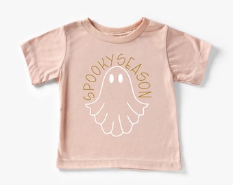 Könnte beinhalten: Ein hellrosa T-Shirt mit kurzen Ärmeln zeigt einen weißen Geist mit zwei Augen und den Text "Spooky Season" in goldenen Buchstaben.