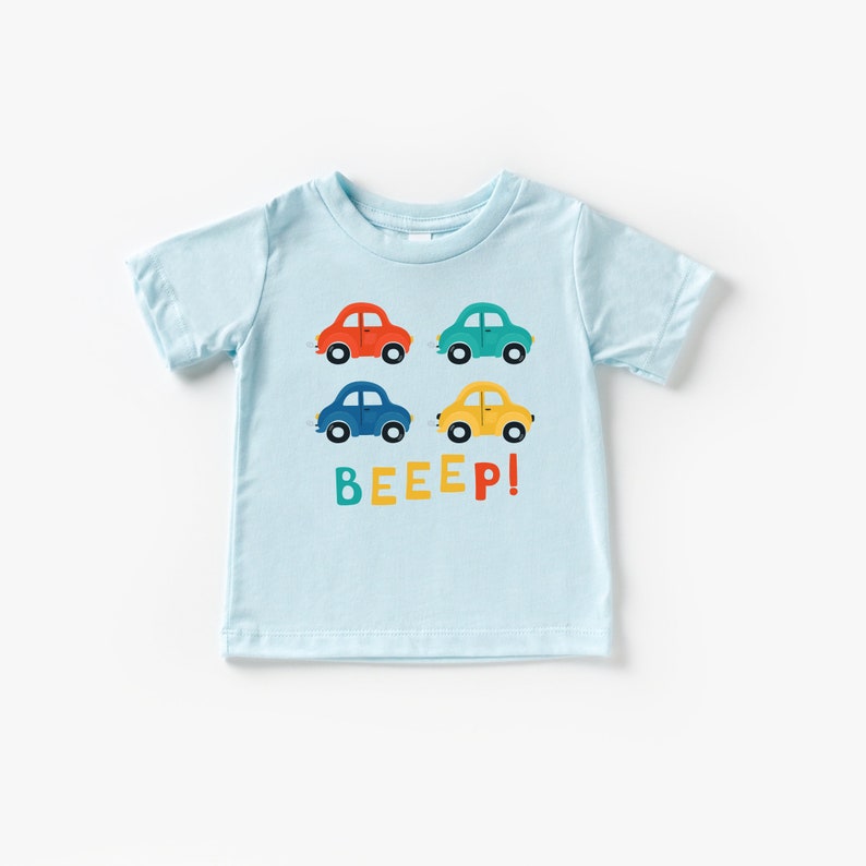 May include: Light blue short-sleeved t-shirt with a graphic of four colourful cars and the word "BEEEP!" in rainbow letters.